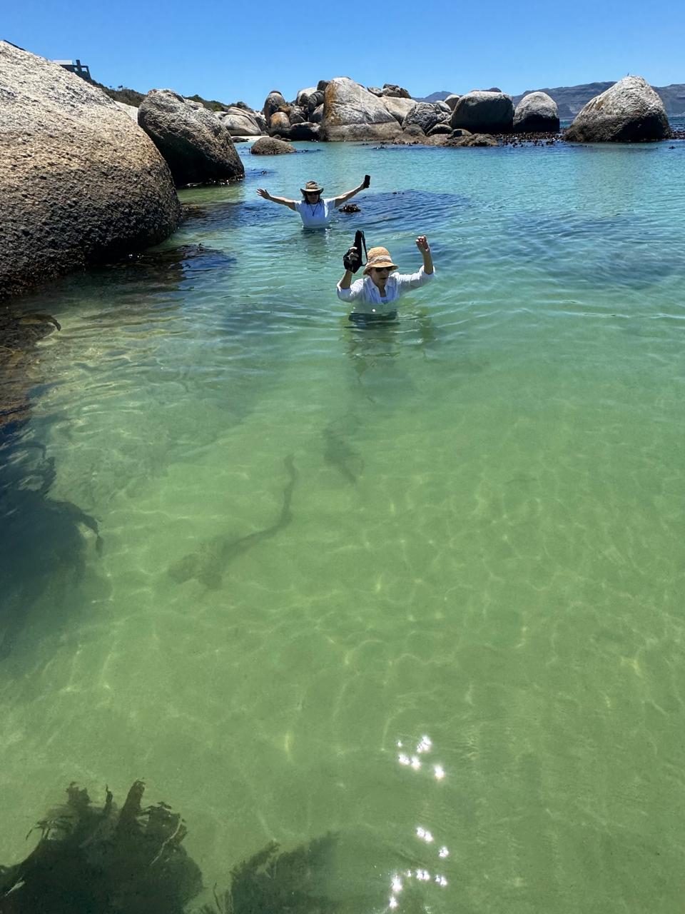Two swimmers with arms raised in the clear water at Boulders