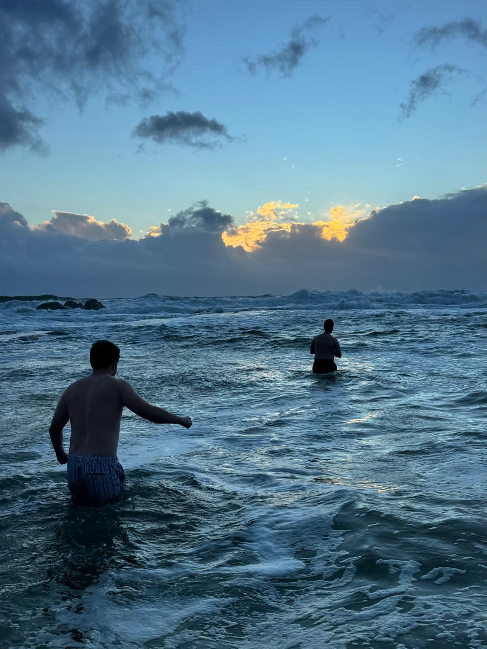 Two swimmers wading into the surf at dusk